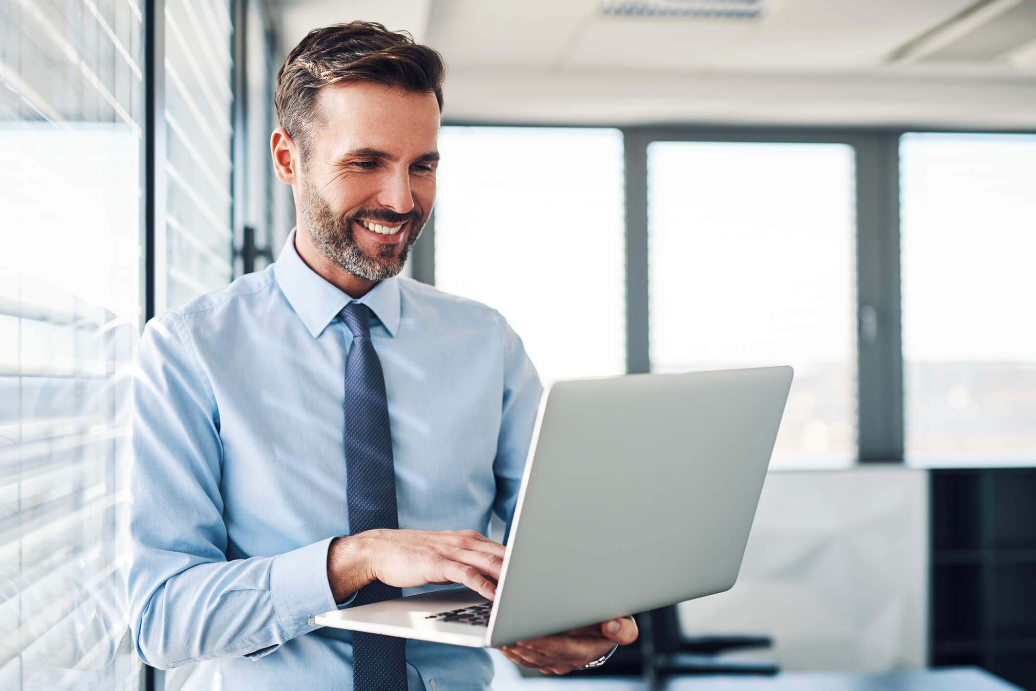 Imagem de um homem do ramo da justiça vestido de roupa social trabalhando feliz em seu laptop.